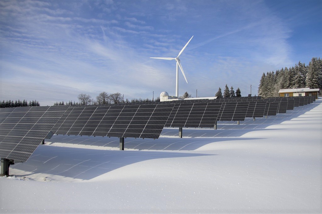 Solar panels on snow with windmill under clear blue sky
